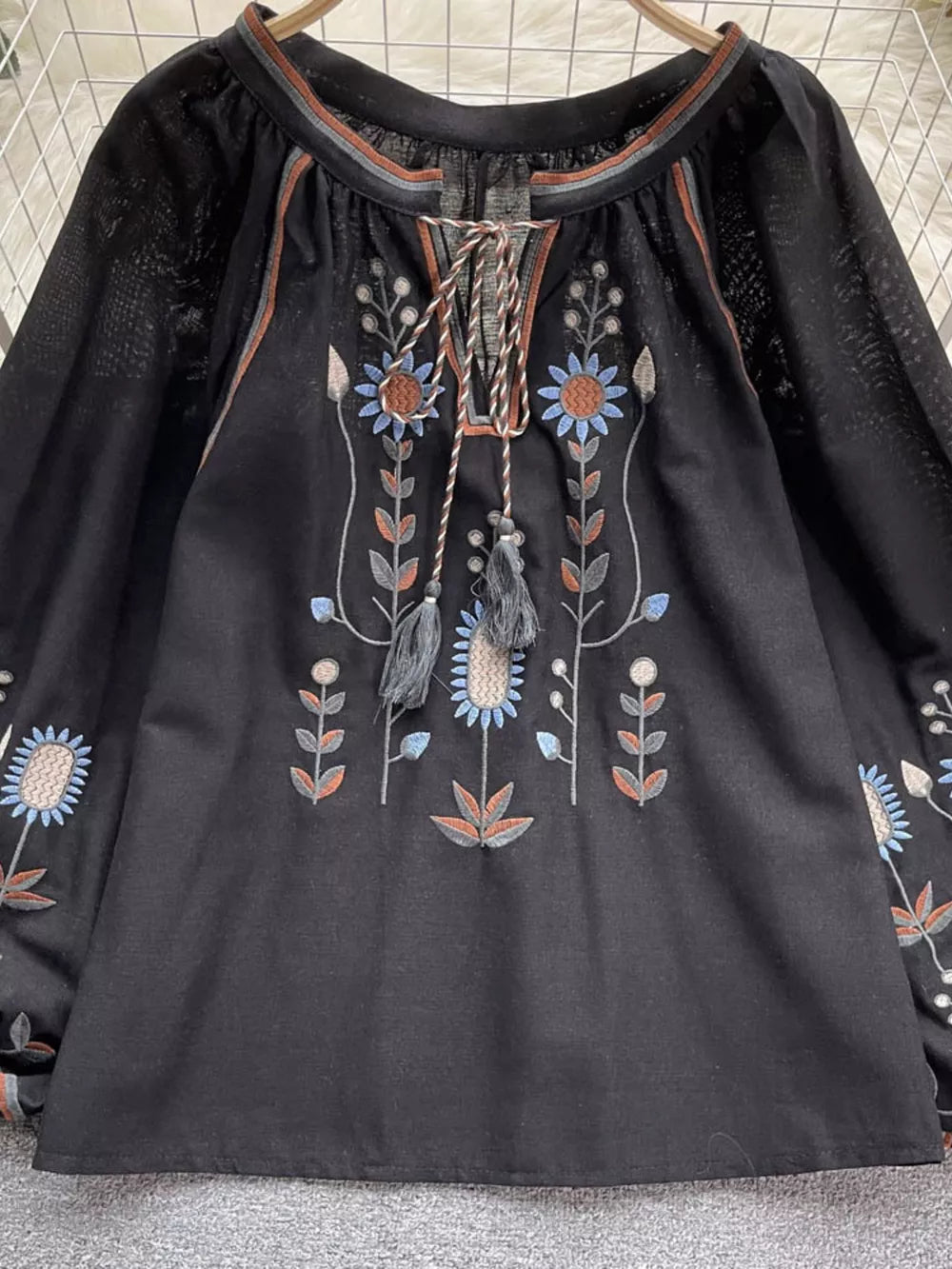 Black tie neck blouse with colorful floral embroidery and billowy sleeves.