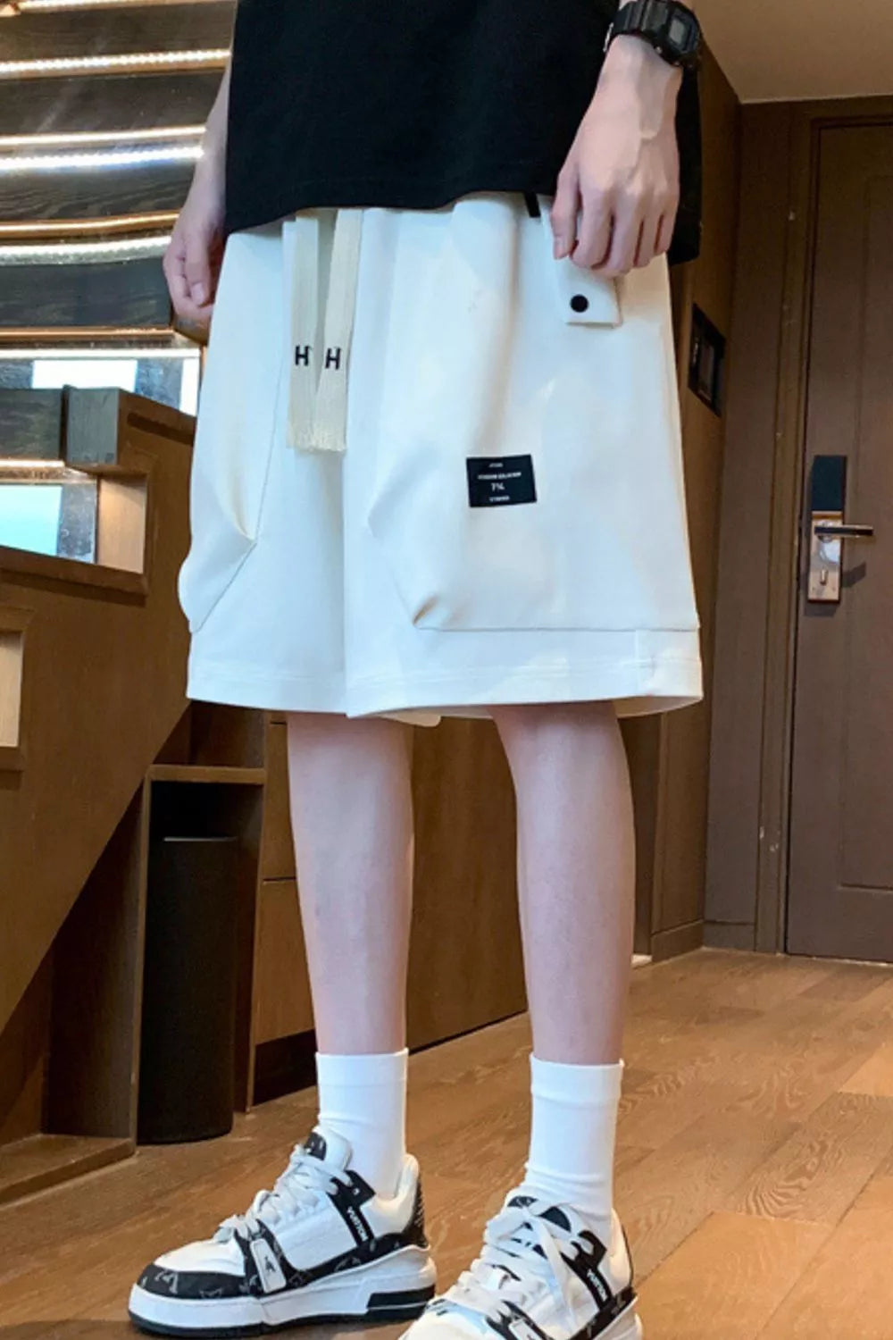 Relaxed fit ivory chino shorts with drawstring and pockets, styled with white socks and sneakers.