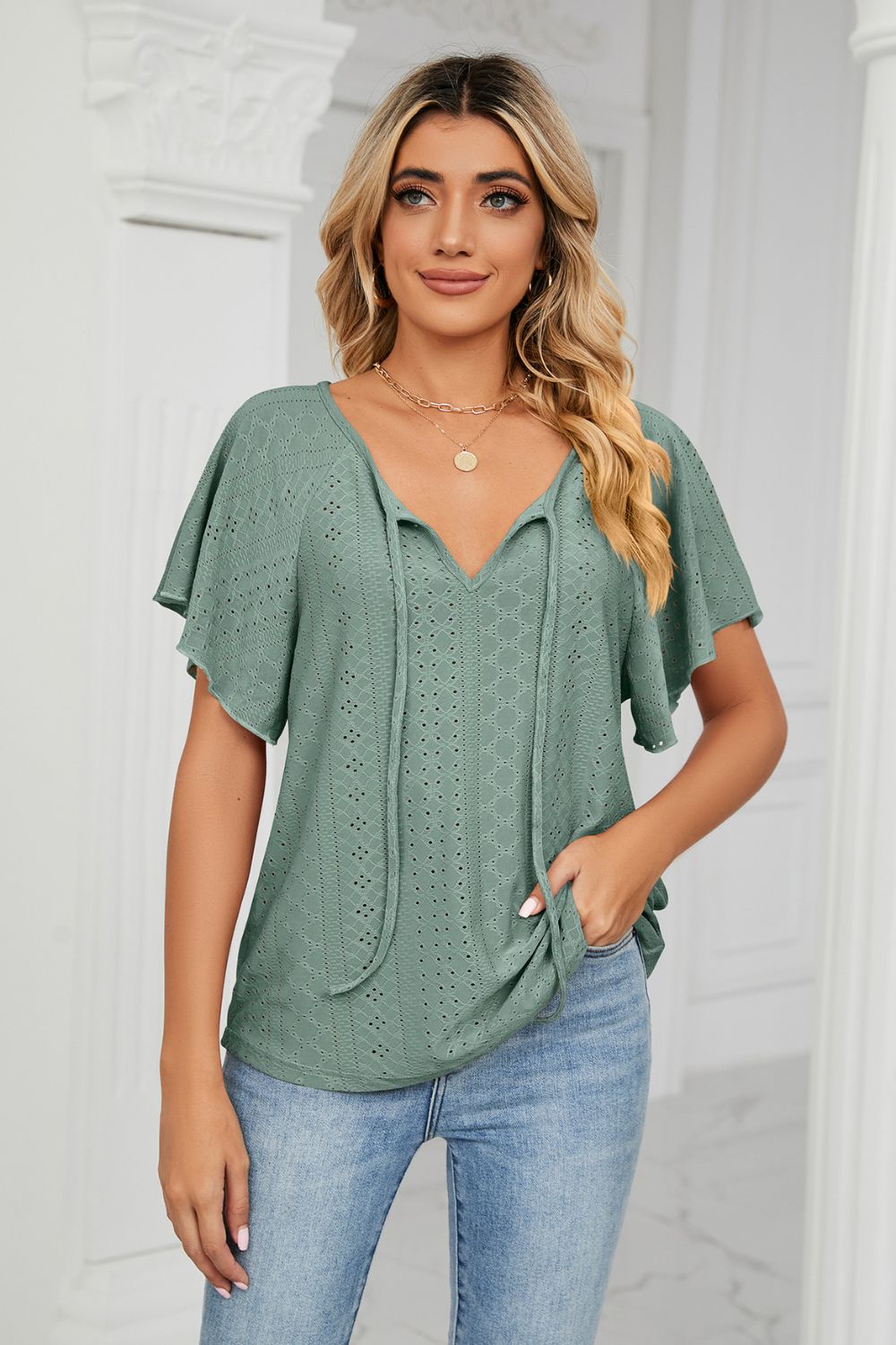 Green eyelet tie-neck blouse with flutter sleeves and a v-neckline.