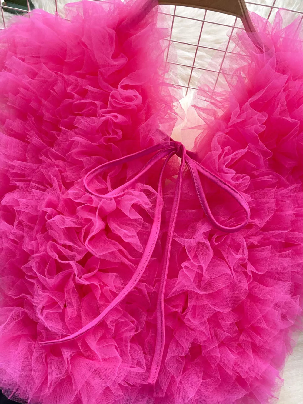 Ruffled V-neck bodysuit in pink with lace detail and bow tie closure.