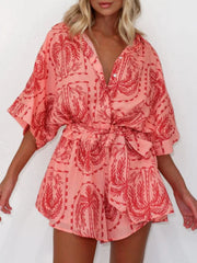 Wrap romper in strawberry with a celestial palm print, short sleeves, and tie waist.