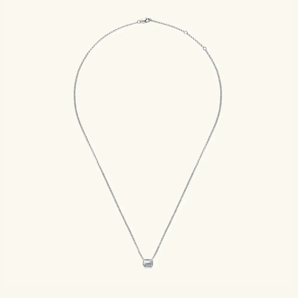 Silver necklace with emerald cut moissanite solitaire pendant and gold bezel.