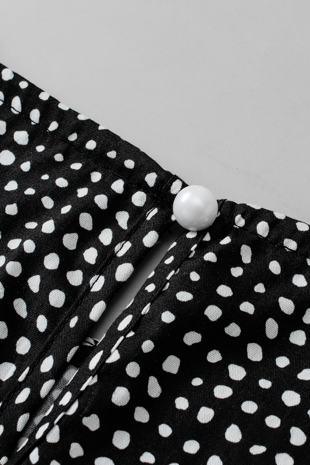Black dotted blouse with a pearl button detail at the neckline.