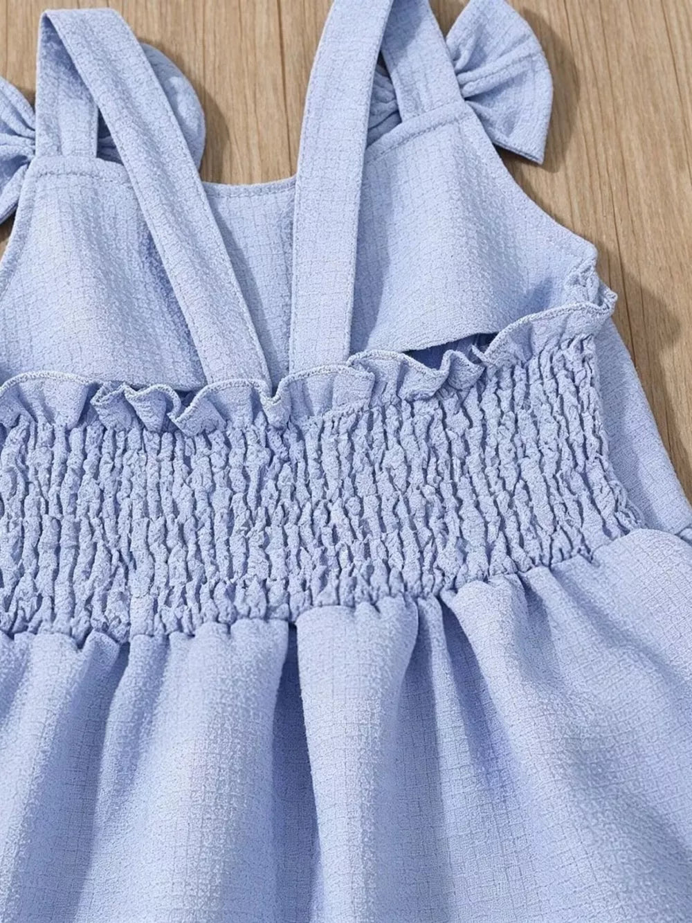 Sky blue baby dress with smocked bodice, ruffle trim, and bow straps.