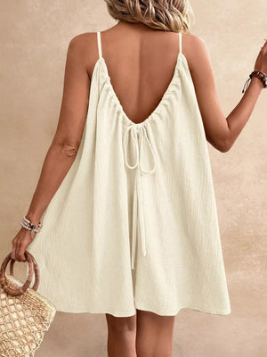 Beige spaghetti strap mini dress with a back tie detail and textured fabric.