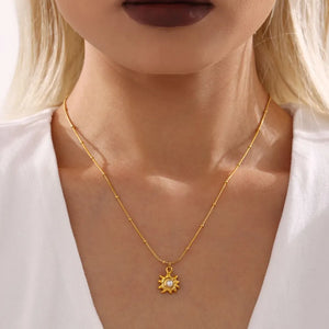 Gold sunburst pendant necklace with pearl detail on a beaded chain.