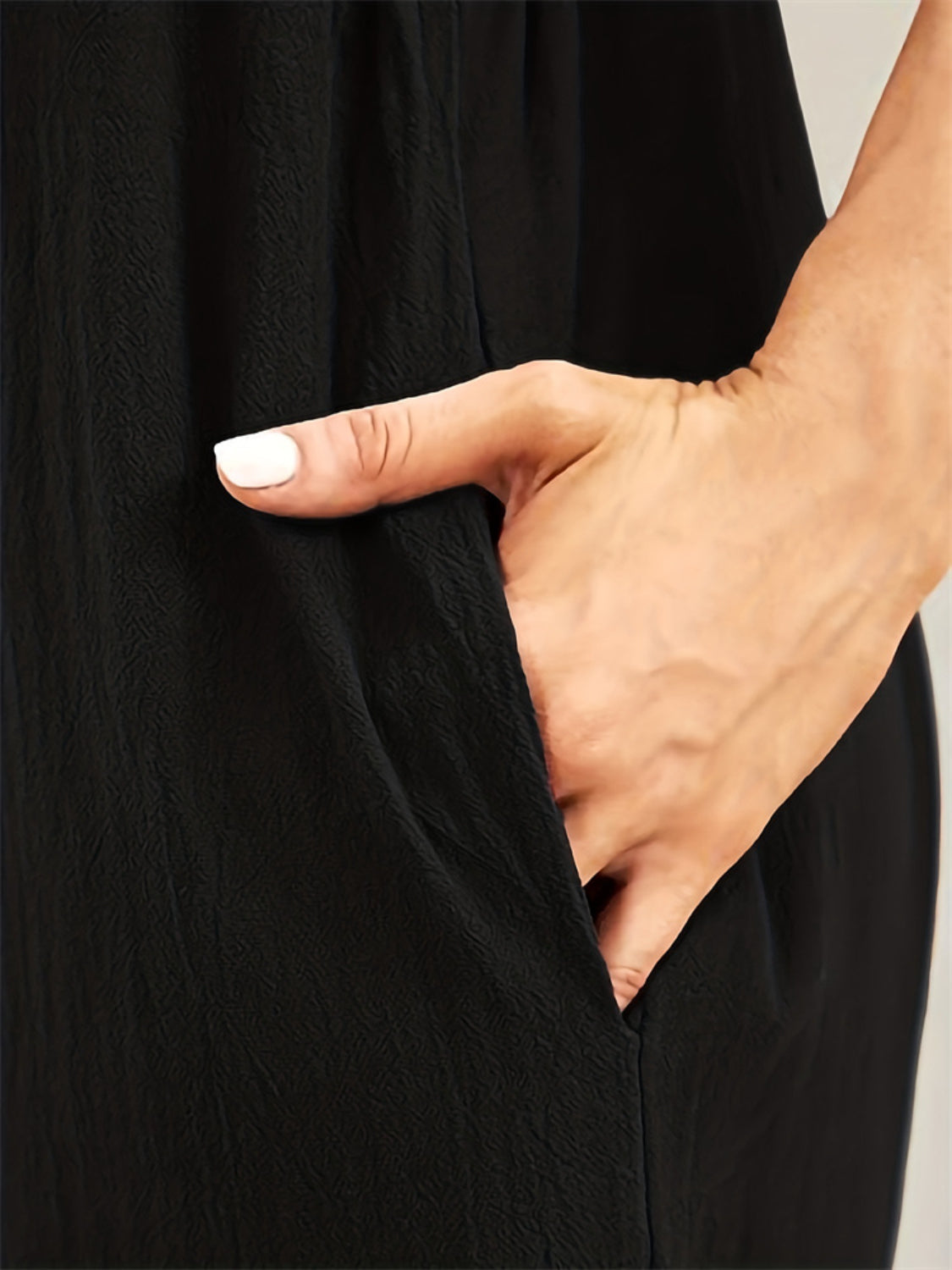 Black cotton overalls jumpsuit with a textured fabric and a hand in the pocket.