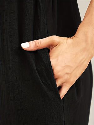 Black cotton overalls jumpsuit with a textured fabric and a hand in the pocket.