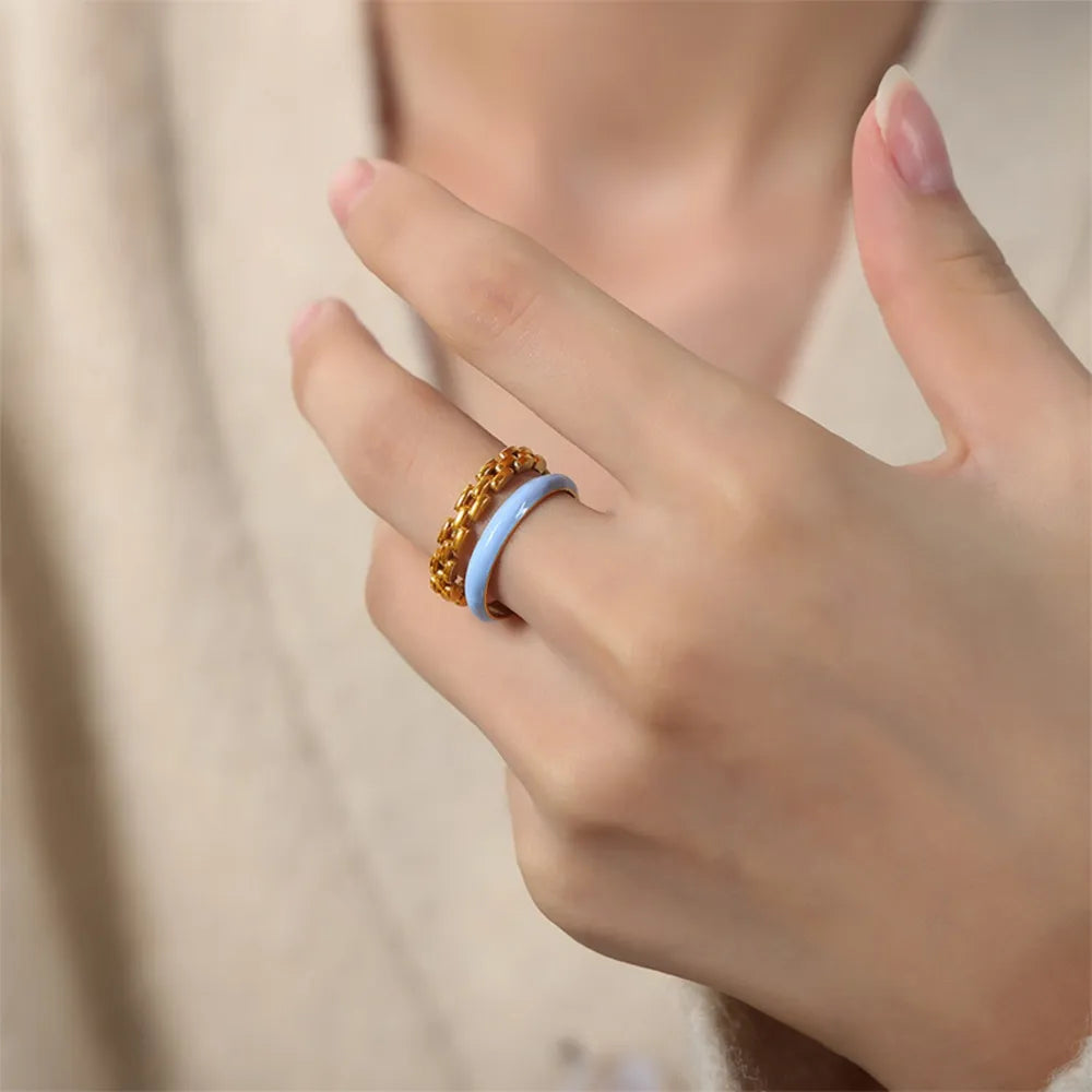 Gold chain link ring stacked with a light blue enamel band ring on a woman's finger.