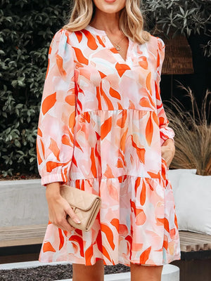 Vibrant abstract print tiered mini dress with V-neck and long sleeves.