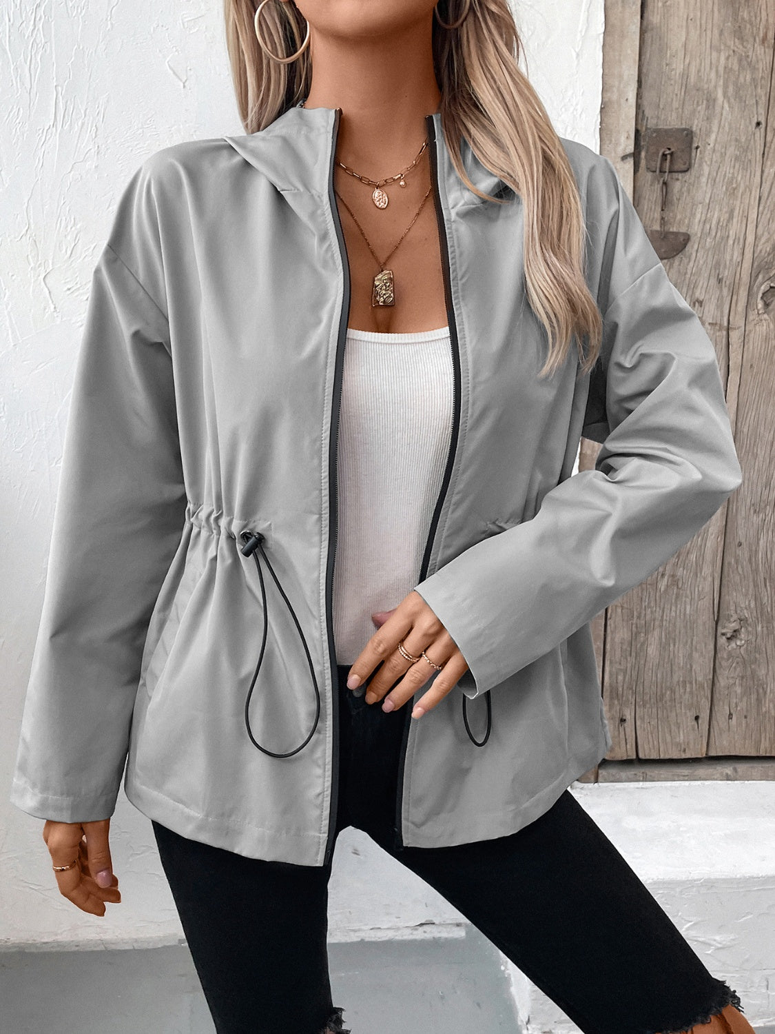 Gray hooded utility jacket with cinched waistline and black trim, worn open over a white tank top.