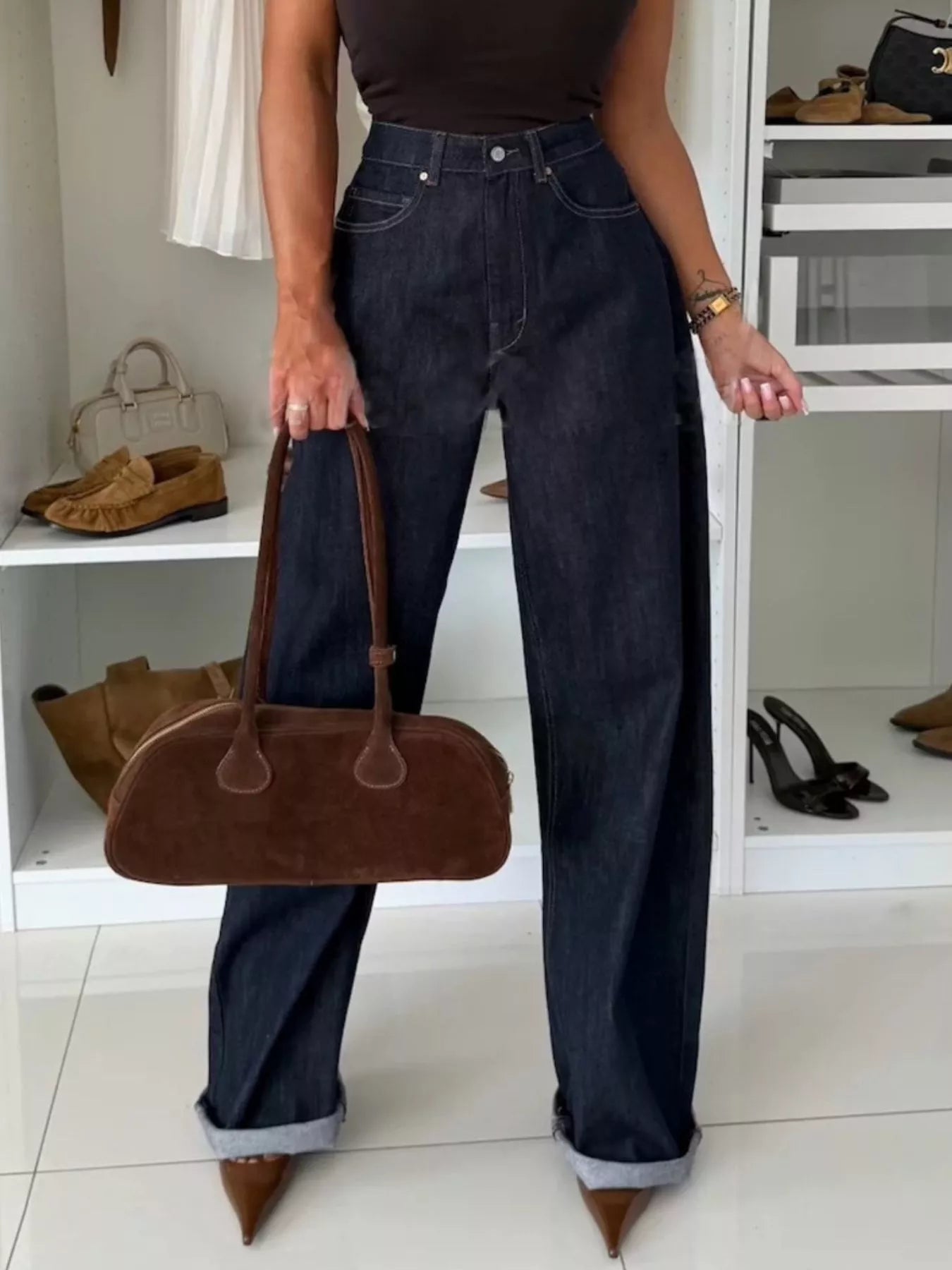 Dark blue denim wide-leg pants with cuffed hems, styled with a brown suede shoulder bag.