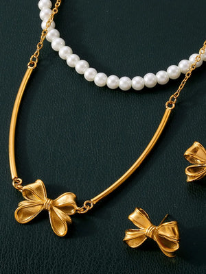 Gold layered necklace with pearl strand and bow pendant, plus matching bow earrings.