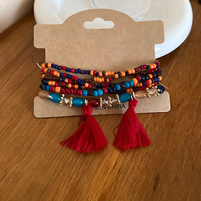 Beaded tassel stacked bracelet set with red tassels and mixed bead colors.