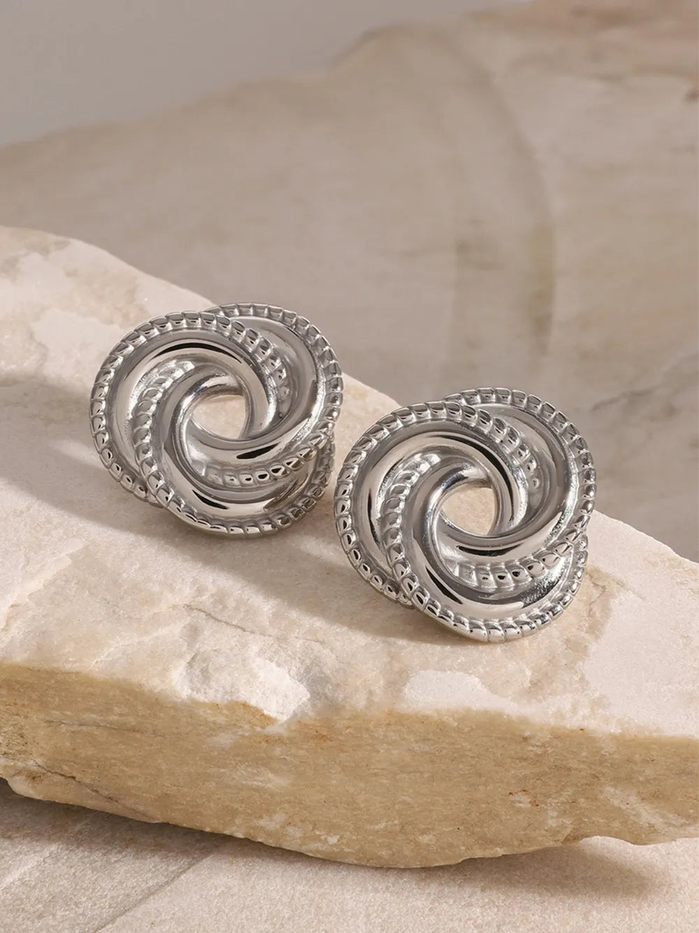 Silver swirl knot stud earrings with textured rope edge detail.