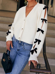 Cream ribbed knit cardigan with split sleeves and black bow details.
