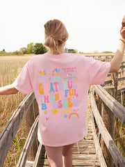 Pink graphic tee with "Grateful Than Blessed" text and colorful affirmations.