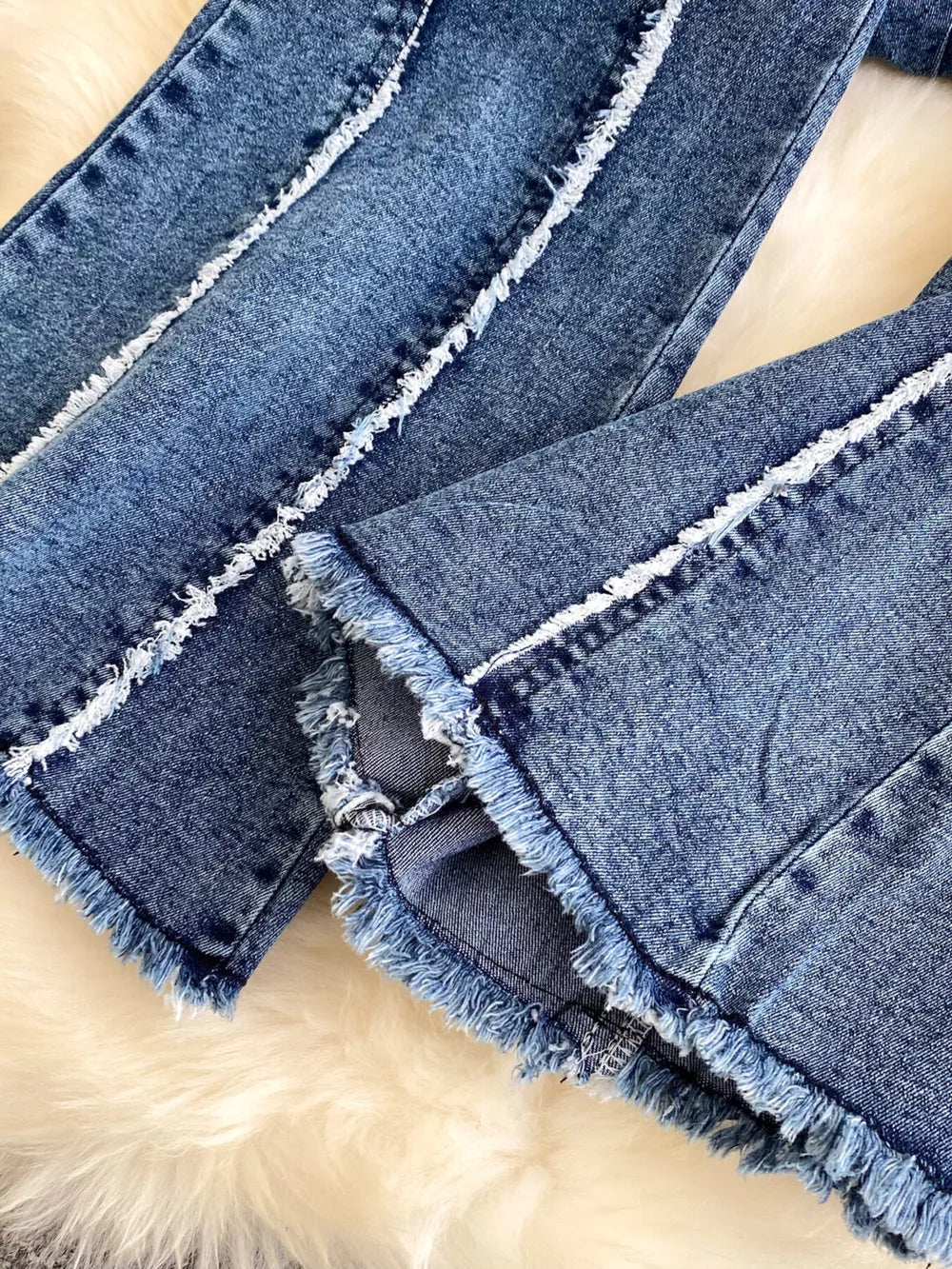 Denim flare pants with raw hem and white contrast stitching detail.