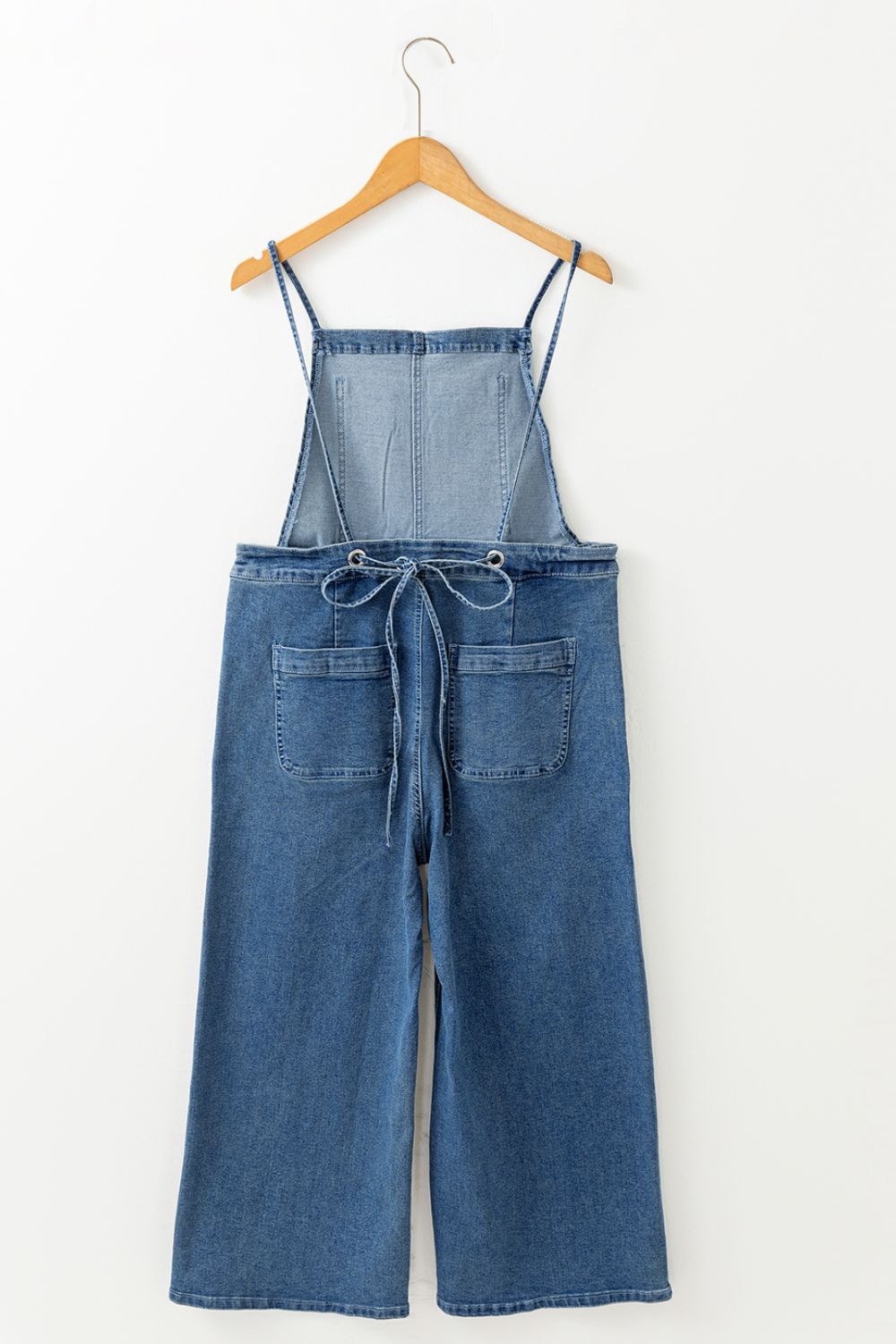Denim wide-leg overalls in medium wash with adjustable straps and tie back detail.