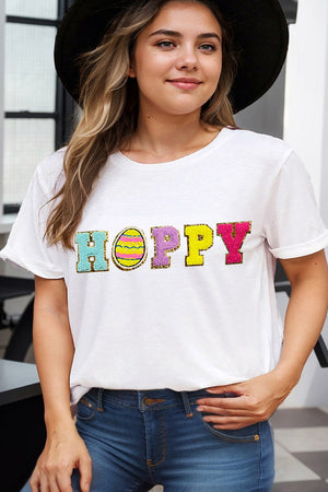 White t-shirt with sequin Hoppy graphic featuring an Easter egg and colorful letters.