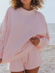 Blush pink crew neck sweatshirt and shorts lounge set on a beach.