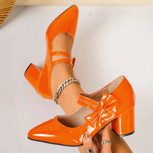 Orange patent leather pumps with pointed toe, block heel, ankle strap, and bow detail.