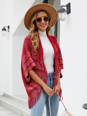Textured red fringe capelet with striped pattern and open front, styled with a white turtleneck and jeans.