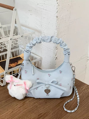 Blue ruched mini crossbody bag with floral print, bow charm, and fluffy pom pom keychain.
