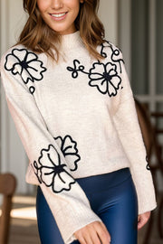 Cream mock neck knit sweater with black embroidered floral details.