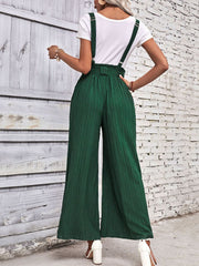 Dark green wide-leg suspender jumpsuit with tie waist and textured fabric.