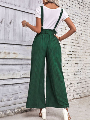 Dark green wide-leg suspender jumpsuit with tie waist and textured fabric.