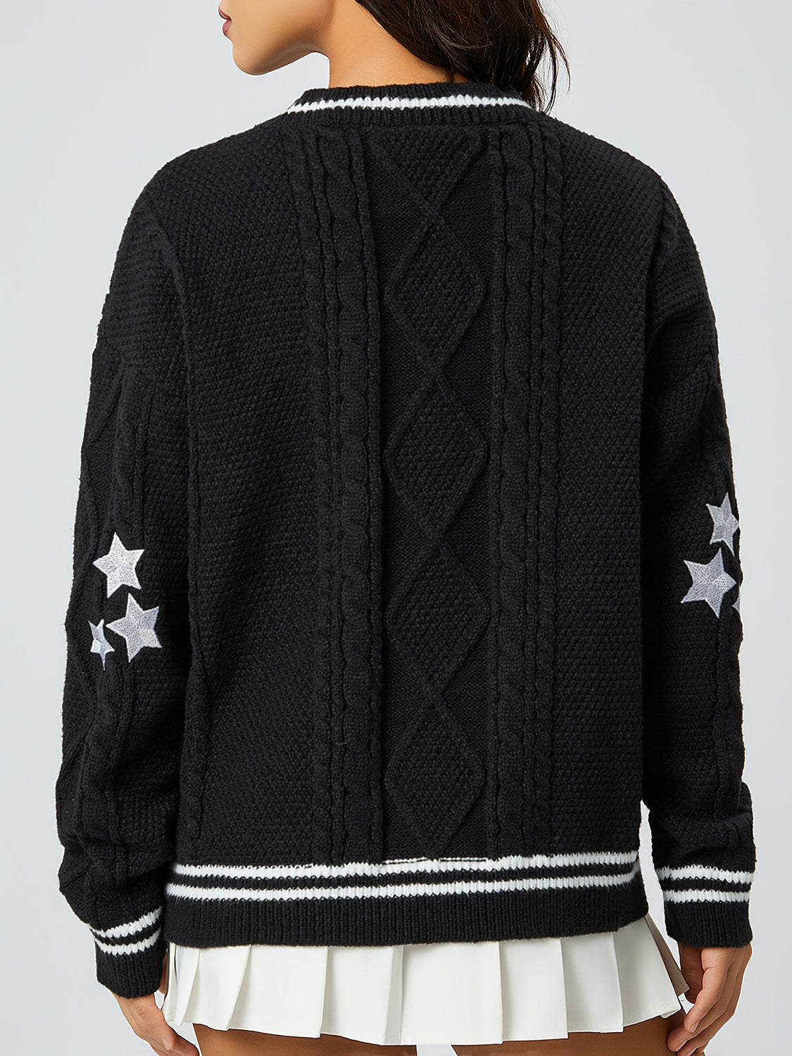 Black cable knit cardigan with white stars on sleeve and striped trim.