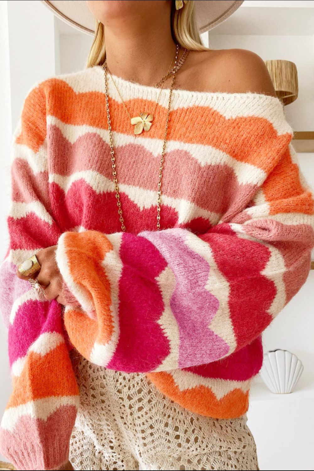 Off-the-shoulder sweater with scalloped stripe pattern in pink, orange, and white acrylic knit.
