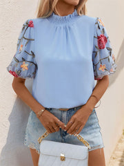Light blue blouse with floral embroidered organza puff sleeves and ruffled mock neck.
