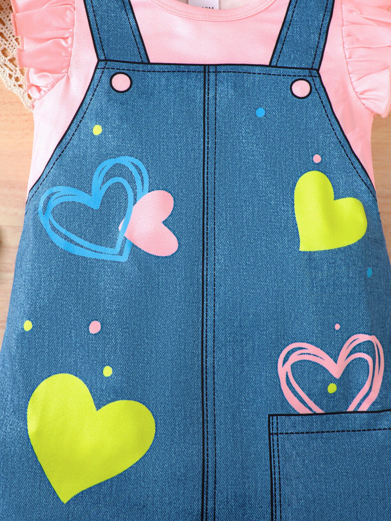 Baby denim overall dress with pink ruffle sleeves and heart print.