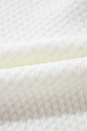 White knit sweater with a textured diamond pattern, made of acrylic.