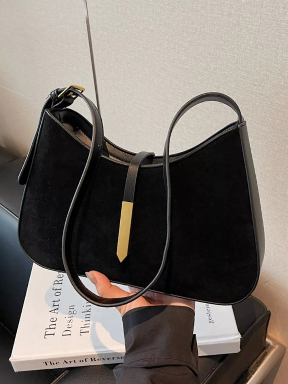 Black suede and leather shoulder bag with curved shape and gold accent detail.