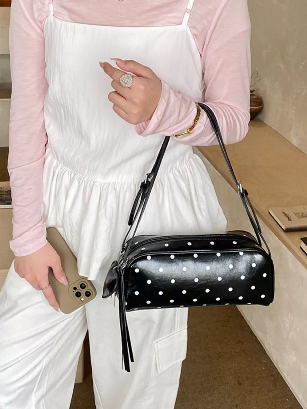 Black polka dot shoulder bag with adjustable strap and tassel detail.
