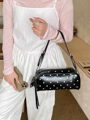 Black polka dot shoulder bag with adjustable strap and tassel detail.