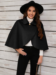 Black asymmetric cape jacket with button front and collar, styled with a hat and turtleneck.