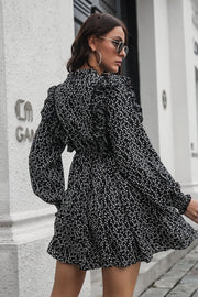 Black dot print dress with ruffle trim, long sleeves, and cinched waist.