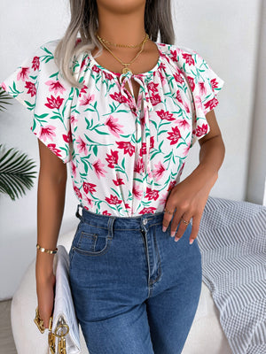 White floral ruffle sleeve tie-neck blouse with pink flowers and green leaves.