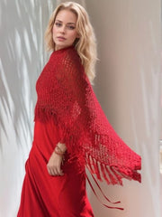 Deep red open-knit poncho with fringe trim and boat neck, styled over a dress.