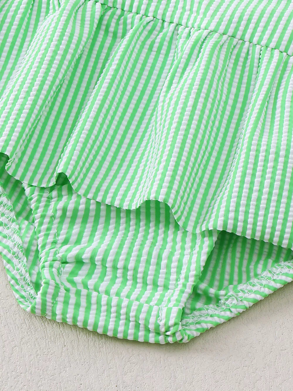 Green striped seersucker one-piece swimsuit with ruffles and a bow detail.