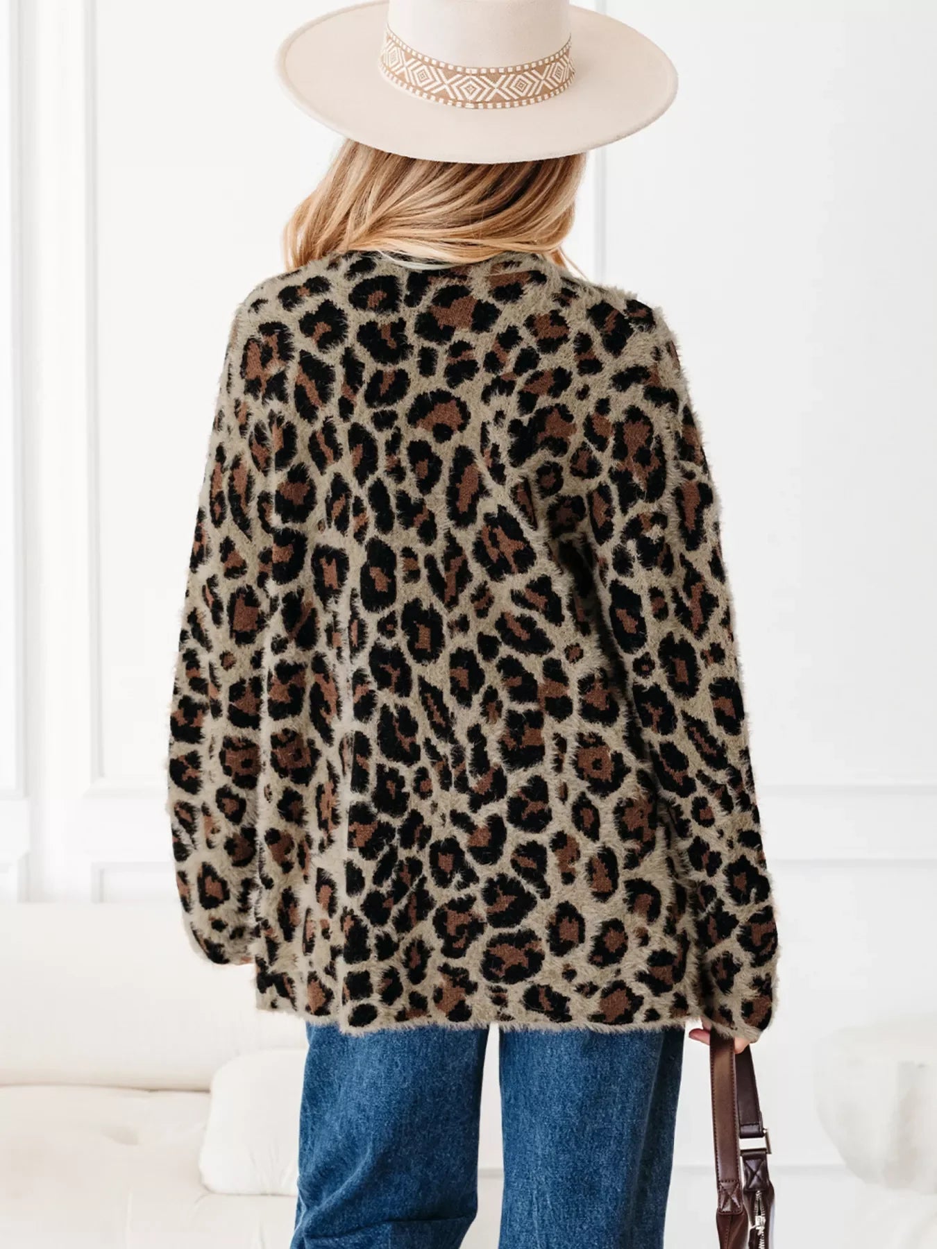 Leopard print fuzzy cardigan with long sleeves and pockets, styled with jeans and a hat.