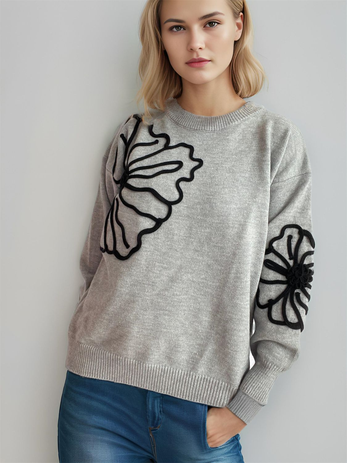 Gray knit sweater with black floral applique on chest and sleeve