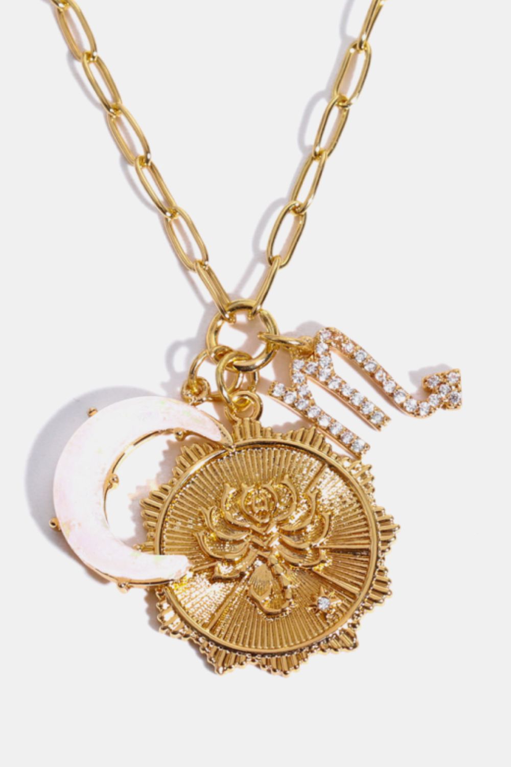 Gold pendant necklace with celestial charms, including a moon, rose coin, and diamond initial.