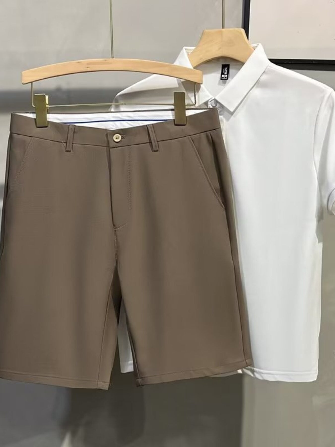 Men's brown chino shorts with a button and zip fly, shown with a white polo shirt.