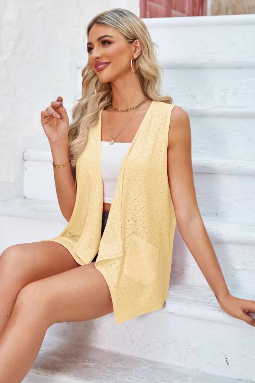 Yellow eyelet vest with pockets and drape front, styled open over a white top.
