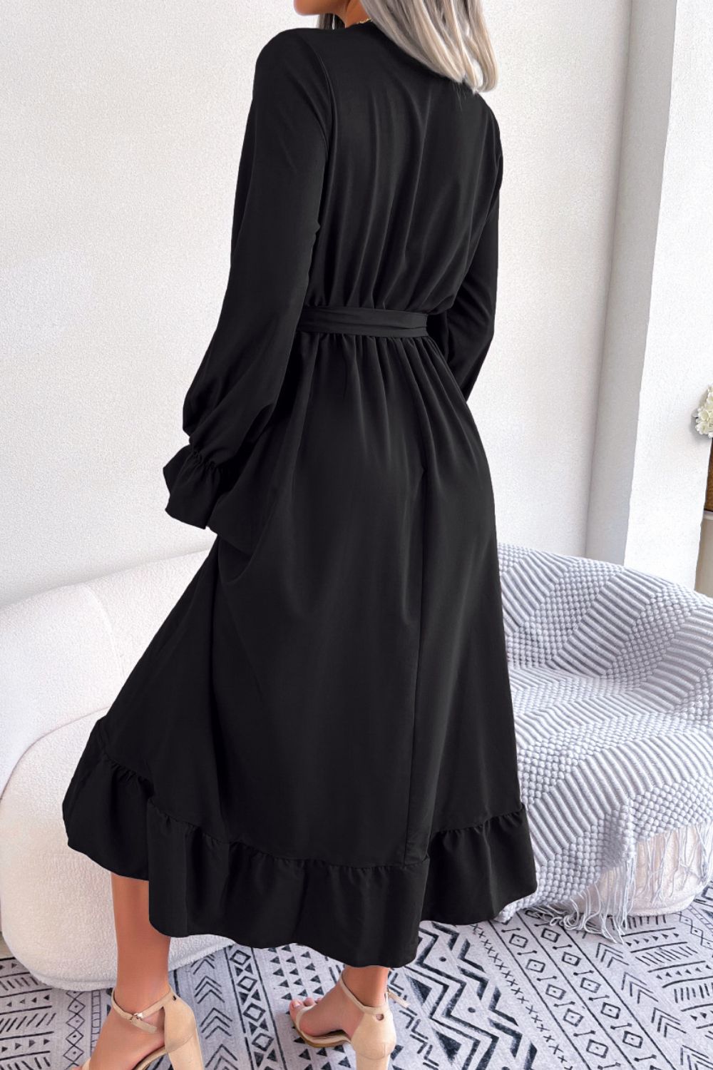 Black midi dress with tie waist, ruffled hem, and long sleeves.